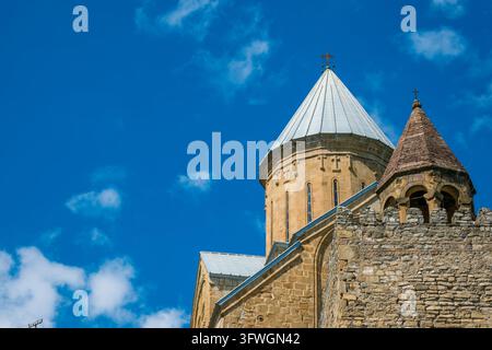 Die Kirchtürme der Festung Ananuri erheben sich über Steinmauern, verzierte Kreuze, kegelförmige Dächer und einen lebendigen blauen bewölkten Himmel in Georgien Stockfoto