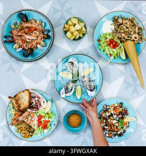 Überblick über Meeresfrüchtegerichte inklusive Austern, Risotto und Salat auf blauen Keramiktellern. Stockfoto