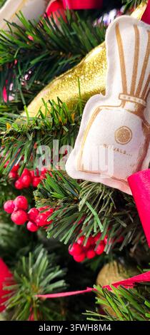 Nahaufnahme eines Stoff-Weihnachtsbaumschmucks mit einem bedruckten Rituals-Flaschenmotiv, umgeben von künstlichen Kiefernzweigen. Stockfoto