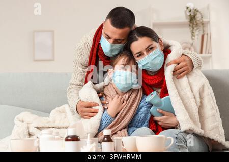 Familien-Gesundheitskrise und saisonale Krankheit, Eltern und Kind tragen medizinische Masken mit Decken und einer Wärmflasche zu Hause während der Grippesaison Stockfoto