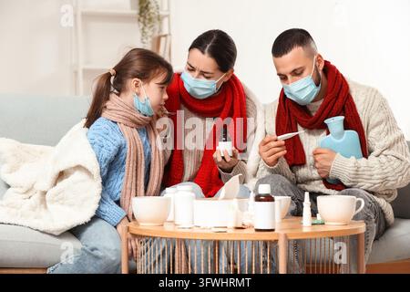 Familien-Gesundheitsversorgung und Grippesaison, Eltern und Kind tragen Gesichtsmasken mit Medikamenten und Thermometer zu Hause während der Genesungsphase im Winter Stockfoto