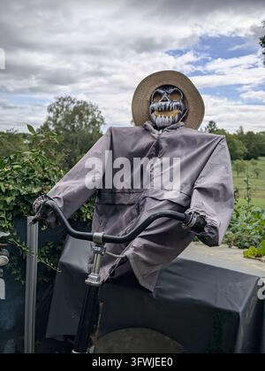 Vogelscheuche-Figur auf Fahrrad im Garten mit Totenkopfmaske und Strohhut unter Wolken Stockfoto