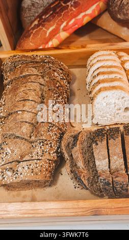 verschiedene geschnittene Vollkorn-, Saaten- und Weißbrotsorten, die in einer hölzernen Bäckerei-Vitrine ausgestellt sind. Stockfoto