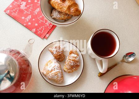 Frisch gebackene Croissants, Sfogliatelle, süße Gebäckstücke, heißer roter Beeren-Tee, Teekanne, Flat Lay. Gemütlicher Morgen, festliche Winterästhetik, Slow-Living-Konzept Stockfoto