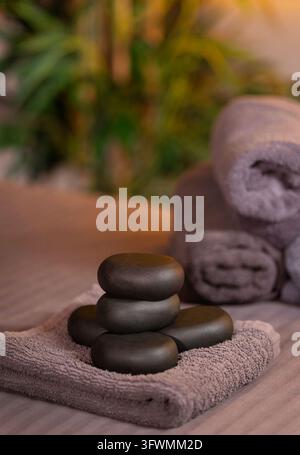 Heiße Steinmassage mit schwarzen Basaltsteinen auf weichem Handtuch in entspannender Spa-Atmosphäre Stockfoto