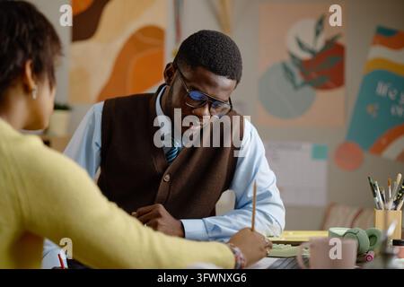 Schwarzer männlicher Tutor unterstützt einen Teenager beim Hausaufgabenmachen im Klassenzimmer Stockfoto