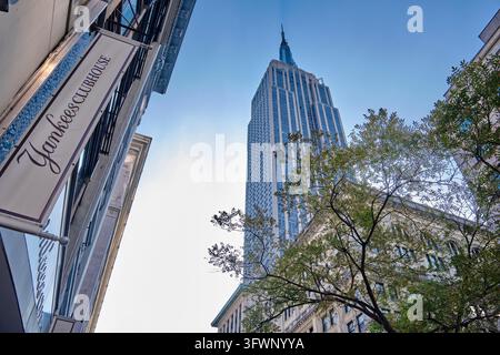 Empire State Building mit dem dämmerungsartigen Schatten des Turms und dem Yankees Clubhouse Shop auf der anderen Straßenseite Stockfoto