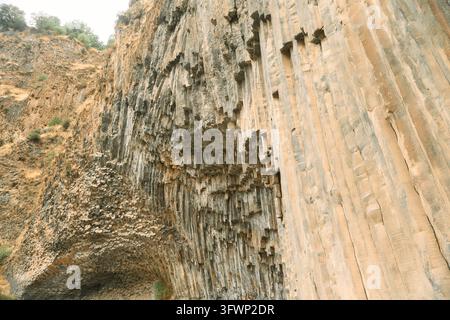 Basalt-Säulenklippe mit sechseckigen vertikalen Felsformationen und schroffen Überhängen in warmen Brauntönen und Grautönen, spärliche trockene Vegetation am oberen Hang Stockfoto