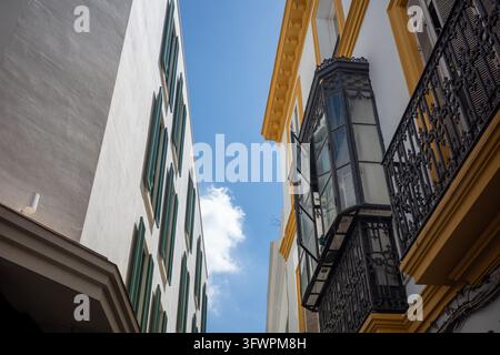 Straßenzufahrt nach oben in Sevilla, Spanien, mit farbenfrohen historischen Fassaden, grünen Fensterläden, kunstvollem schmiedeeisernem Balkon, geschlossenem Erkerfenster und hell Stockfoto