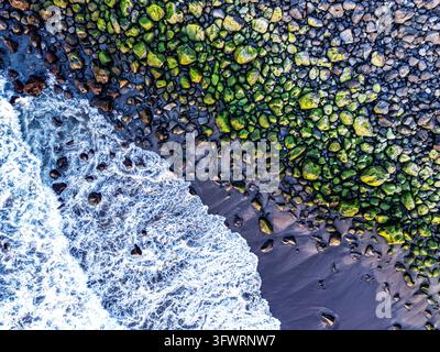 Luftbild von moosbedeckten Felsen an einem dunklen Vulkanstrand mit brandenden Meereswellen in den Azoren, Portugal. Stockfoto