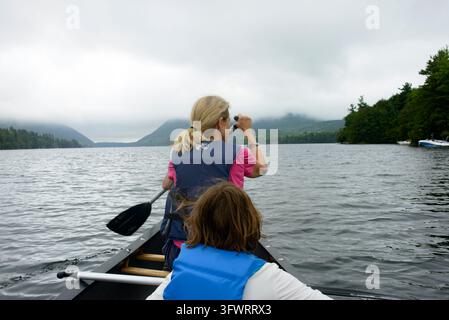 Rückansicht von Mutter und Kind, die auf einem See an einem bewölkten Tag Kanu paddeln Stockfoto