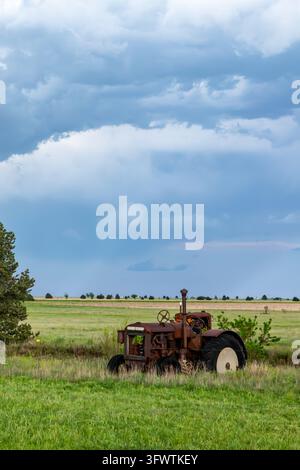 Ansicht eines alten rostigen Traktors, der in einem grasbewachsenen Feld unter einem dramatischen bewölkten Himmel in Oklahoma City, Oklahoma, USA, verlassen liegt. Stockfoto