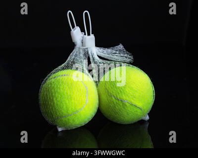 Gelber Tennisball im Netzpaket auf schwarzem Hintergrund mit Reflektion Stockfoto