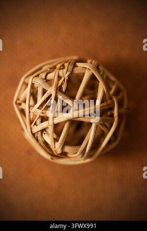 Nahaufnahme eines locker gewebten Weidenballs aus hellen Natursträngen vor einem warmen braunen Hintergrund mit flacher Tiefenschärfe Stockfoto