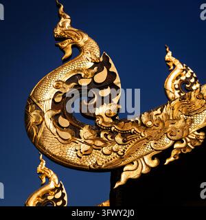 Chiang Mai, Thailand - 17. Januar 2026: Nahaufnahme eines kunstvollen goldenen Naga-Dachgiebels mit aufwendigen Schuppen und Flammenmotiven vor einem klaren… Stockfoto