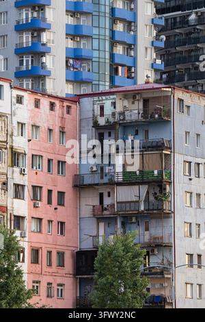 Dichter Wohnblock mit verwitterter Fassade und Balkonen vor modernem Batumi-Wolkenkratzer Stockfoto