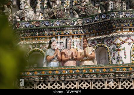 Bangkok, Thailand - 1. Februar 2026: Drei Frauen in traditioneller thailändischer Kleidung stehen mit aneinandergelegten Händen im Gebet vor einem hochrangigen... Stockfoto