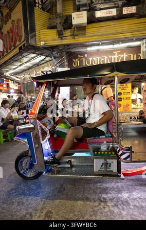 Bangkok, Thailand - 1. Februar 2026: Ein Mann sitzt auf einem farbenfroh geschmückten Tuk-Tuk an einem geschäftigen Nachtmarkt in Bangkok, Thailand. Stockfoto