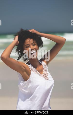 Frau lacht, Hände im Haar, am Strand Stockfoto