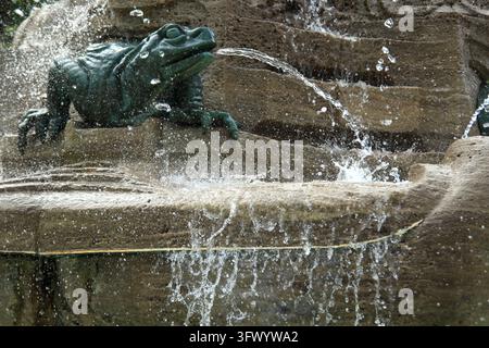 Bronzene Frosch-Brunnen-Skulptur, umgeben von dynamisch spritzendem Wasser in einem historischen Steinbrunnen. Wassermotion, detaillierte Texturen und lebhafte Wassereffekte Stockfoto