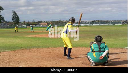 Verschiedene weibliche Softballspielerinnen, die auf einem lokalen Feld spielen, Schlagspielerin schwingt den Schläger auf einen Softball in der Luft Stockfoto