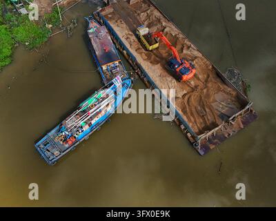 Luftaufnahme eines Baggers, der Sand auf ein großes Schleppkahn auf einem Fluss lädt, mit einem kleineren Boot, das daneben festgemacht ist, in Sambas, Westkalimantan, Indonesien. Stockfoto