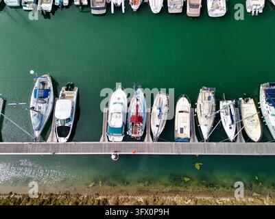 Luftaufnahme von oben verschiedener Segelboote und Motoryachten, die entlang eines hölzernen schwimmenden Piers in einem ruhigen Marina-Becken vertäut sind. Stockfoto