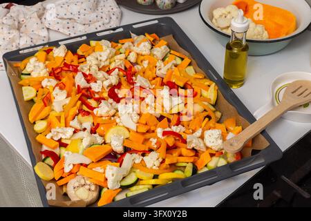 Auberginen, Zucchini, Karotten, Zwiebeln, Knoblauch, Blumenkohl und Paprika backen auf einem Blech im Ofen während der Mahlzeitvorbereitung zu Hause. Stockfoto