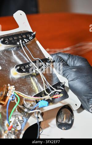 die Hände eines Gitarrenbauers, die mit einem Marker Details auf dem weißen Körper einer E-Gitarre hervorheben und markieren. Stockfoto