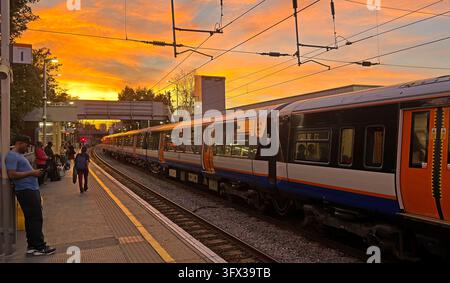 London TfL Overground-Zug und wartende Passagiere am Bahnhof Hackney Central unter einem lebhaften orangefarbenen Sonnenuntergang im Osten Londons Stockfoto