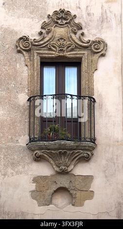 Verschnörkeltes Barockfenster an einer alten Gebäudemauer mit einem kleinen Balkon und aufwendigen Steinschnitzereien Stockfoto