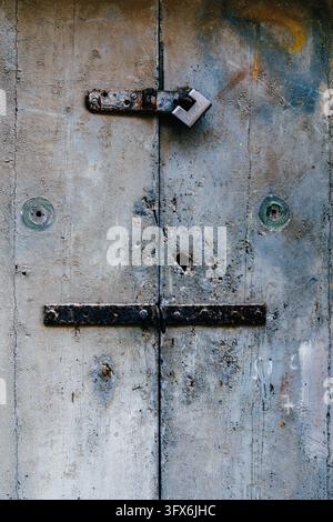 Grau gestrichene Holzhaustür mit eisernem Riegel, altem Vorhängeschloss, rostigen Scharnieren und Schlüssellöchern Stockfoto