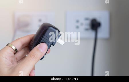 Einsetzen eines schwarzen elektrischen Steckers mit einer Frauenhand in eine weiße Plastiksteckdose an einer Wand. Schließen Sie den Stromstecker an. Stockfoto