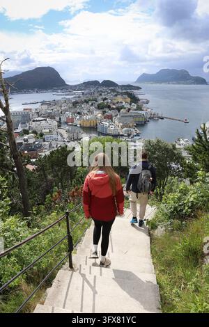 Junges Paar geht die Treppe vom Aksla-Aussichtspunkt hinunter mit einem Panoramablick auf Ålesund in Norwegen. Touristen steigen steinerne Stufen hinab, während sie t Stockfoto