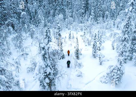 Zwei Wanderer in heller Winterkleidung gehen durch einen schneebedeckten Wald nahe Akaslompolo in Lappland, Finnland, umgeben von gefrorenen Bäumen an einem ruhigen W Stockfoto