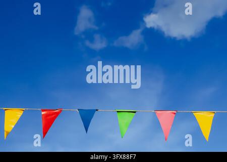 Reihe bunter dreieckiger Wimpel, die an einer Schnur gegen blauen Himmel hängen, mit großem Kopierraum oben, Außendekoration für Festivals. Stockfoto