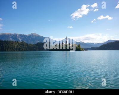 Die Kirche der Himmelfahrt Mariens steht auf der kleinen Insel im Bled-See, während sich die Julischen Alpen dahinter in Slowenien erheben. Stockfoto