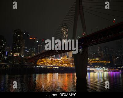 Blick von neben einem Brückenpfeiler auf leuchtende Flussufergebäude bei Nacht. Stockfoto