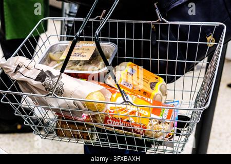 London, UK, 22. Oktober 2026, Nahaufnahme eines Einkaufskorbs, der von einem Kunden in einem britischen Supermarkt getragen wird, mit einer Baguette, geschnittenem Brot, Eiern und einer Fertiggericht Stockfoto
