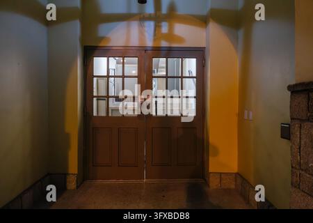 Dramatische Schatten fallen über einen geschlossenen hölzernen Eingang bei Nacht. Stockfoto