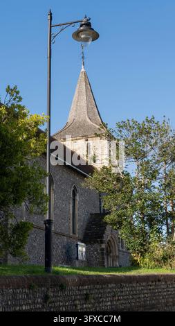 Vertikale Niedrigwinkelaufnahme, die traditionellen Pfarrkirchenturm aus Feuerstein mit hölzernem Schindeldach, gotischen Fenstern und schwarzer Vintage-Laterne zeigt Stockfoto