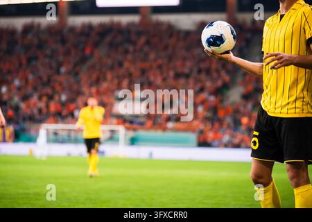 Fußballspieler in gelber Uniform hält einen Ball mit beiden Händen bereit, um einen Einwurf während eines Stadionspiels auszuführen. Stockfoto