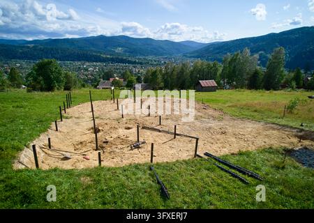 Pfahlfundamentinstallation für den Hausbau in einer ländlichen Berglandschaft, Metallpfosten im Boden gesetzt, die das zukünftige Zuhause markieren, Konzept von Immobilien Stockfoto