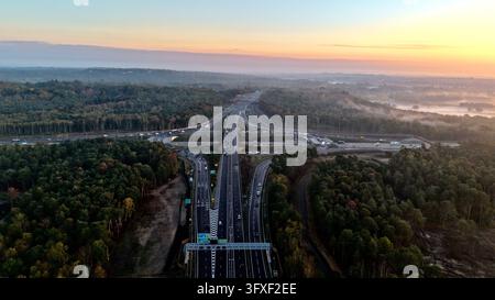 Luftbilddrohnenaufnahme der M25-Abfahrt 10 und der A3-Straßen, umgeben von herbstlichem Wald und Morgennebel in Surrey, England Stockfoto