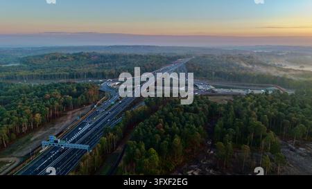 Luftbild-Drohnenaufnahme der A3, die die M25 Junction 10-Autobahnschleife im nebligen Herbstwald von Surrey, England, kreuzt Stockfoto