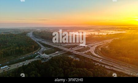 Luftbilddrohnenansicht der M25-Anschlussstelle 10 und der A3-Wisley-Kreuzung bei Sonnenaufgang in Surrey, England Stockfoto