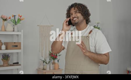 Mann, der das Smartphone am Ohr hält, Hand auf der Brust im Studio-Blumenladen trägt eine Schürze und spricht am Telefon; ruhiger Service. Stockfoto