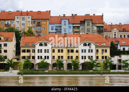 Symmetrische Fassade historischer und moderner Wohnungen mit roten Dächern entlang des renovierten Lent-Ufers an der Drau in Maribor, Slowenien. Stockfoto