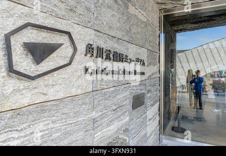 Tokio, Japan, 22. NOV 2024 - Nahaufnahme des Logos und Namens des Kadokawa-Kulturmuseums auf einer strukturierten Steinmauer, mit einem Glaseingang, der einen Besucher reflektiert Stockfoto