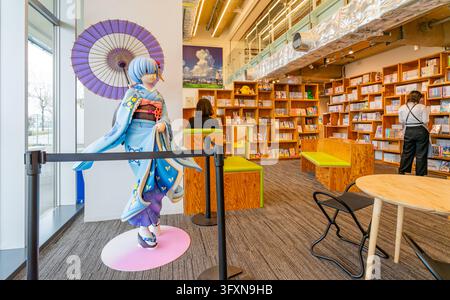 Tokio, Japan, 22. NOV 2024 - Eine lebensgroße Anime-Charakter-Statue, die einen blauen Kimono trägt und einen Sonnenschirm hält, steht in einem modernen Bibliotheksinneren mit Stockfoto